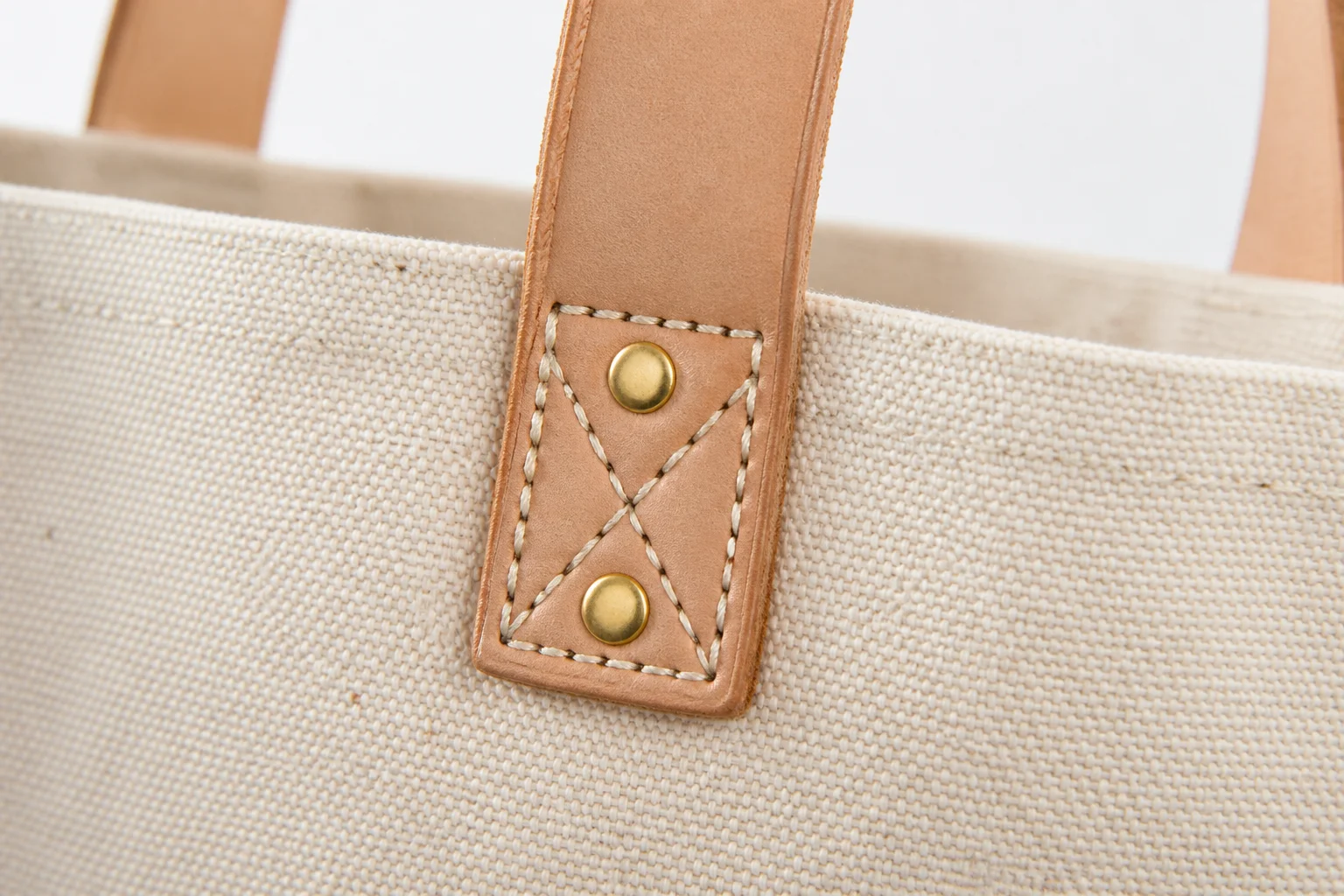 Close-up of a tote bag handle attachment with reinforcement stitching and rivets