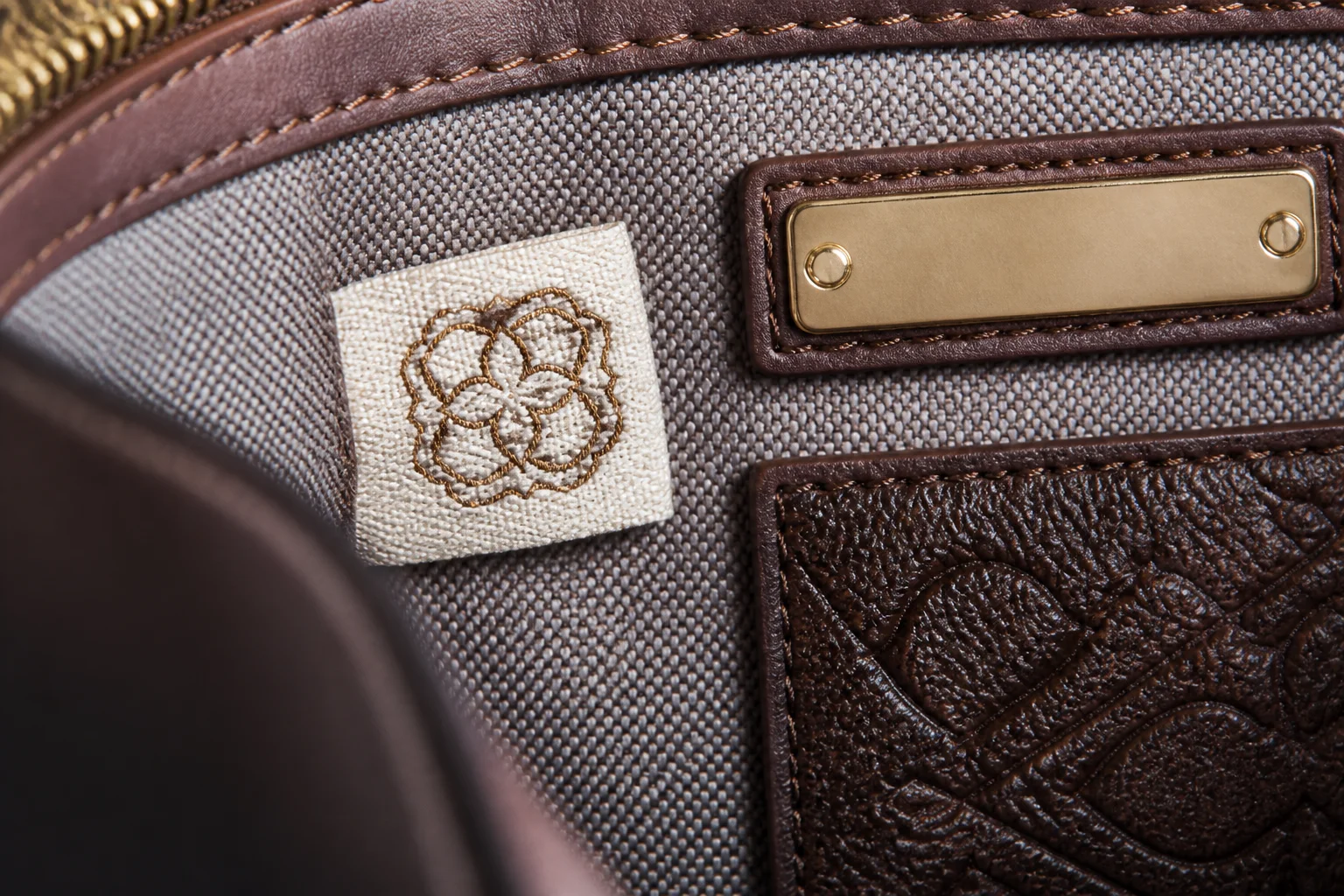 Custom woven brand label sewn into a bag interior seam beside a metal logo plate and embossed patch