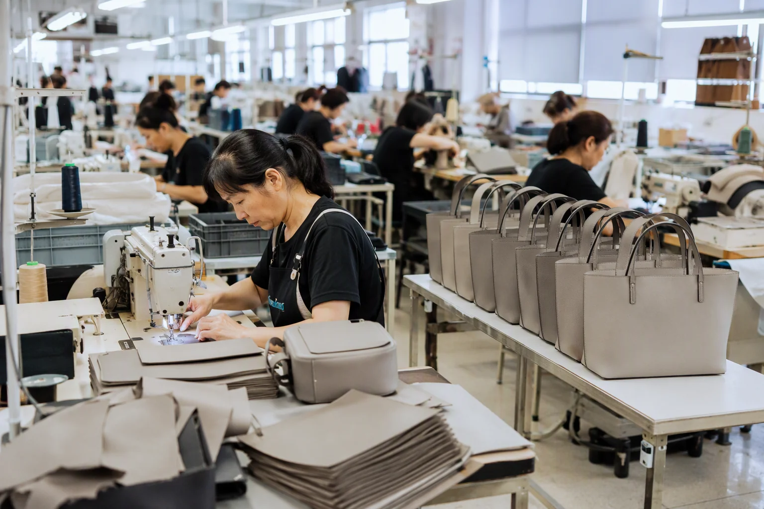 Bag factory production line assembling modern minimalist bags in neutral colours with workers at sewing stations