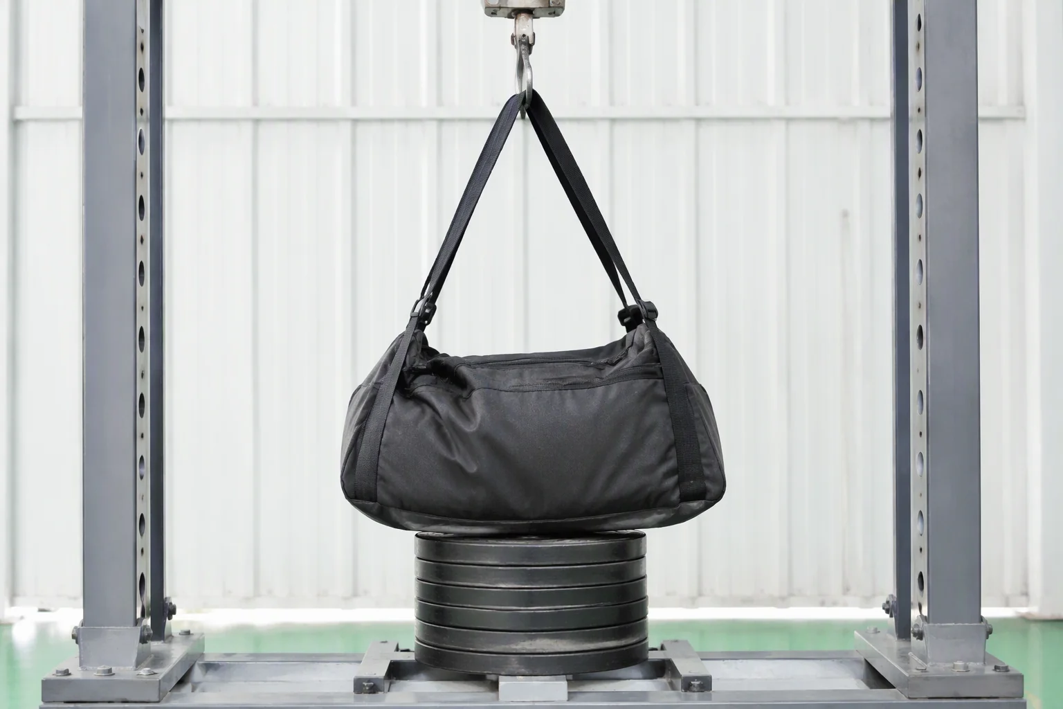 Load test on a bag suspended by its shoulder strap from a steel hook with weighted plates inside