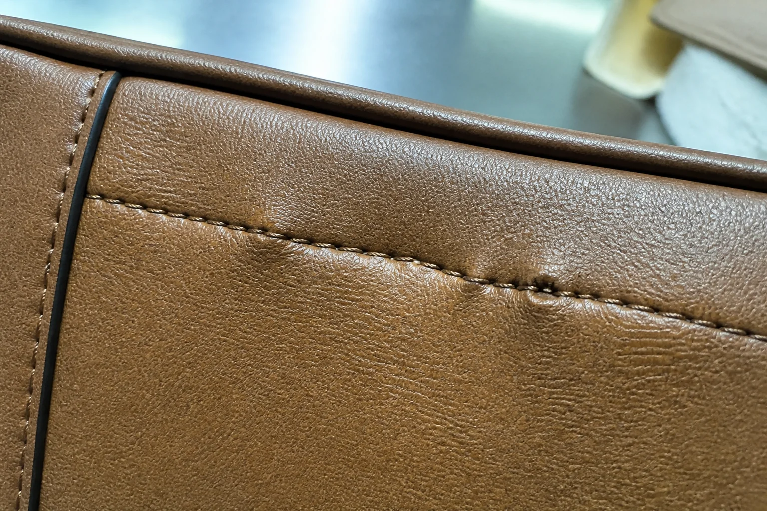 Close-up of an irregular stitch line on a PU leather bag panel showing uneven stitch density and a puckered seam