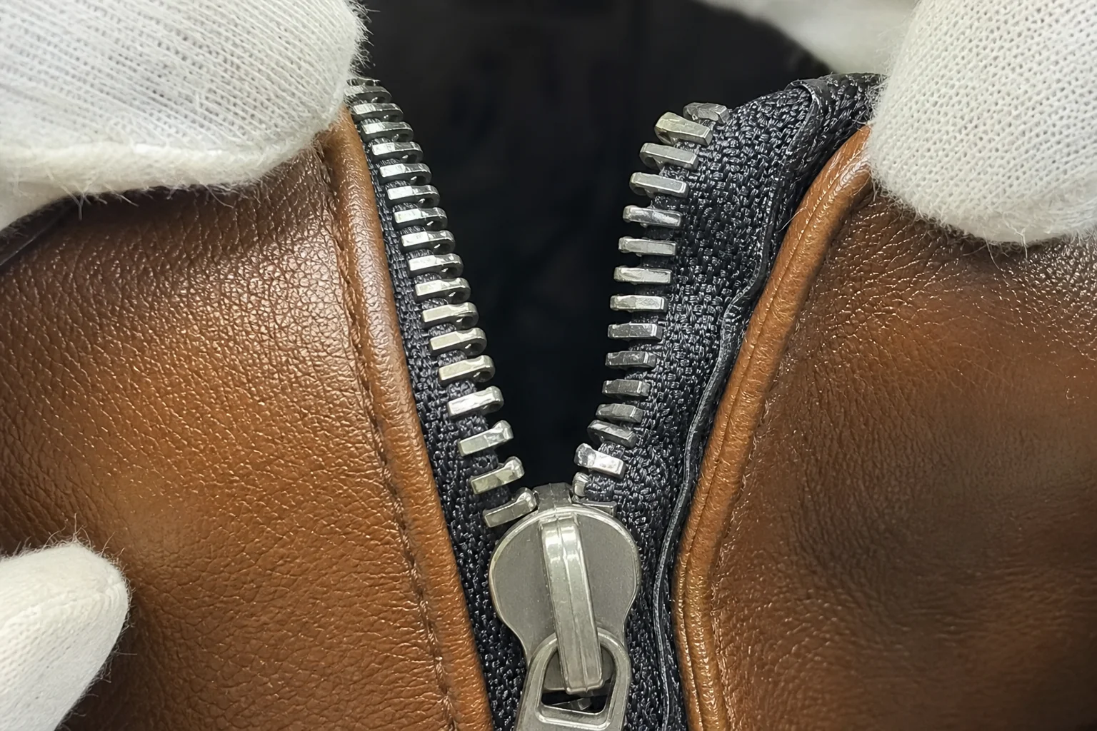 Close-up of a zipper with mismatched teeth and a distorted zip tape on a PU leather bag opening
