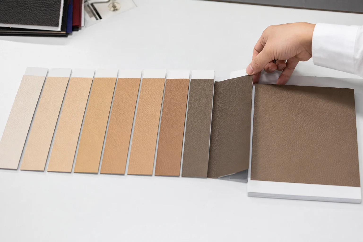 Lab dip colour samples of PU leather laid out in a row beside a master standard swatch on a work table