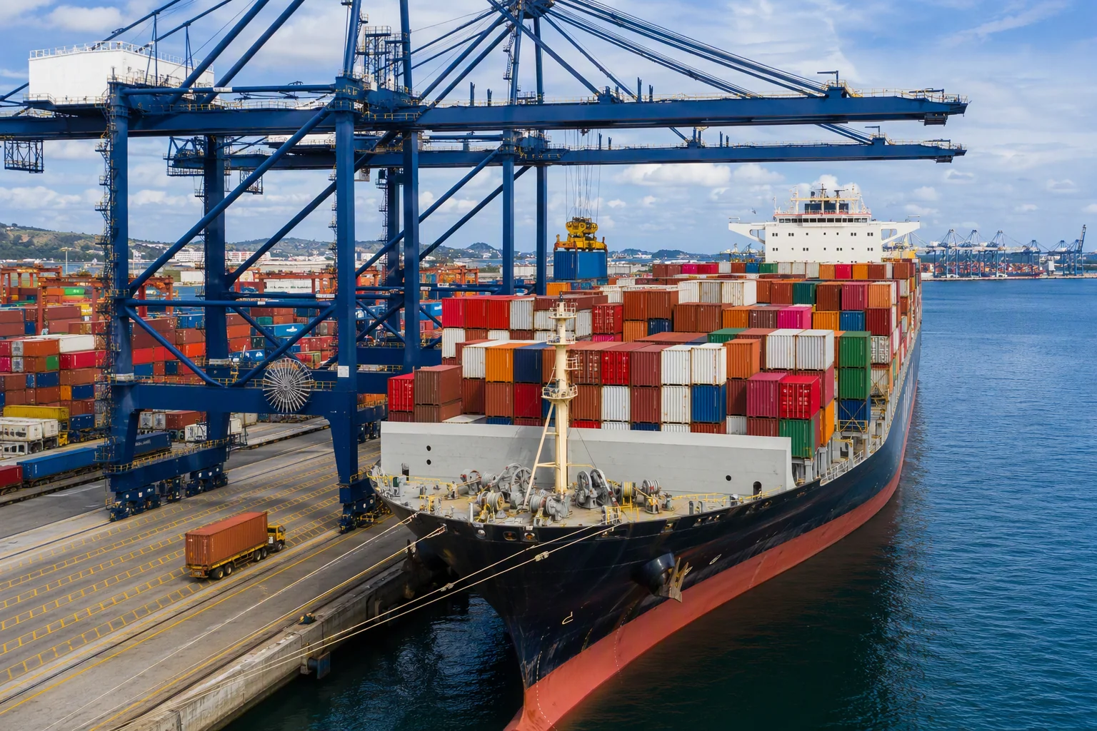 Container ship being unloaded at a port terminal with stacks of import containers and gantry cranes