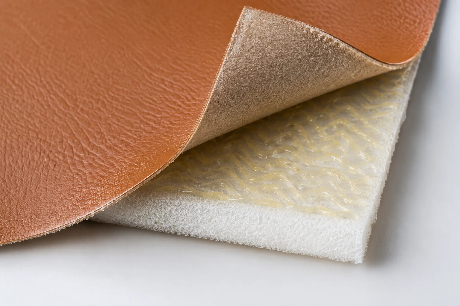 PU leather panel peeled back from a foam interlining to reveal the adhesive bond pattern