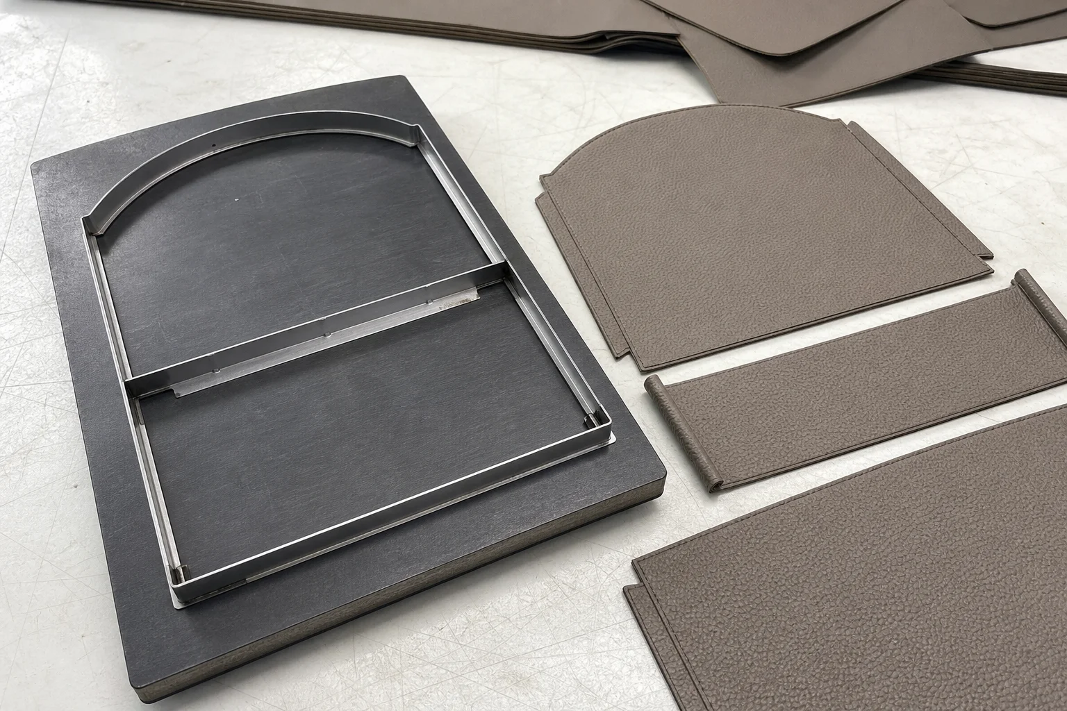 Steel cutting die for a bag panel beside cut PU leather pieces on a workbench