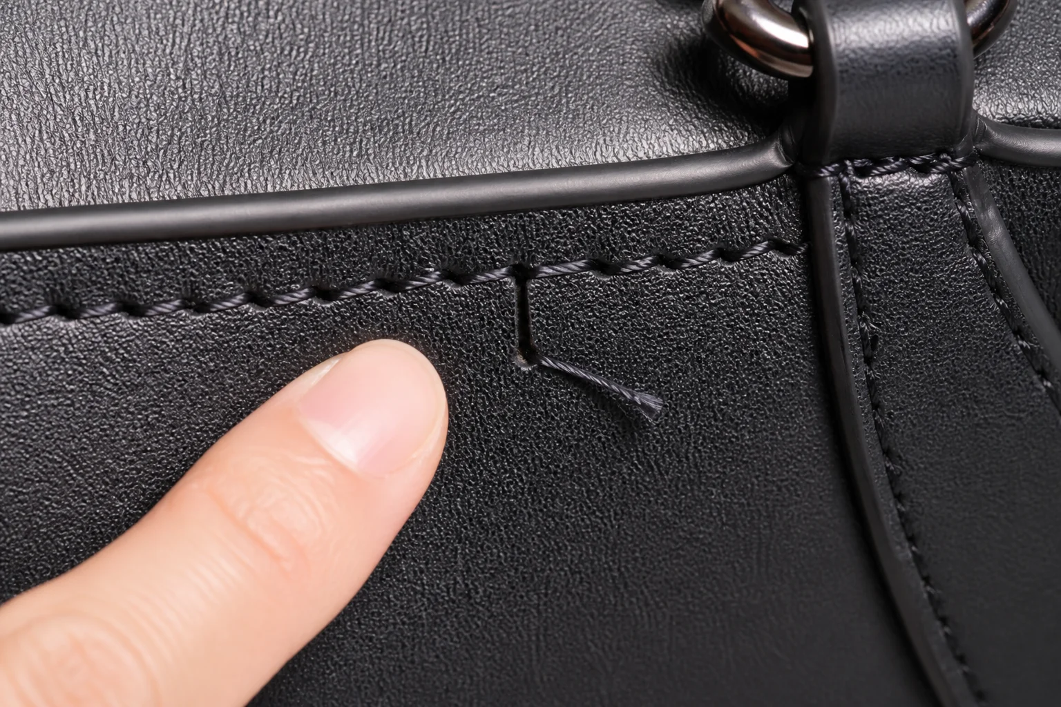 Close-up of an uneven stitch and loose thread end on a PU leather bag seam